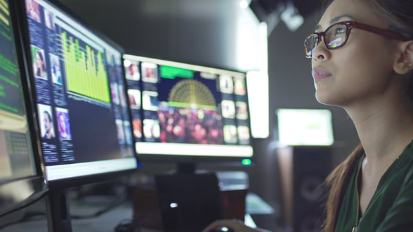 Image of an adult IT worker assessing data profiles on three monitors.