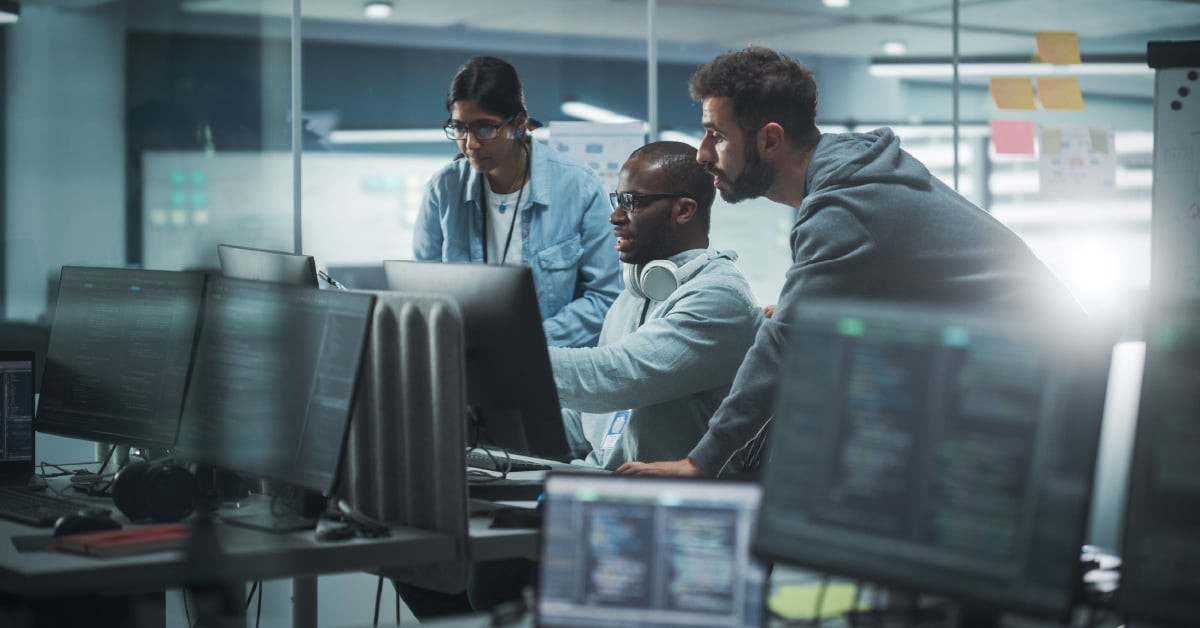 A cybersecurity team gathers around a computer monitor.