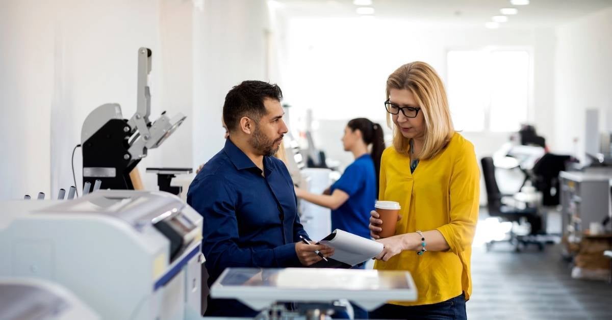 Two coworkers go over production printing costs.