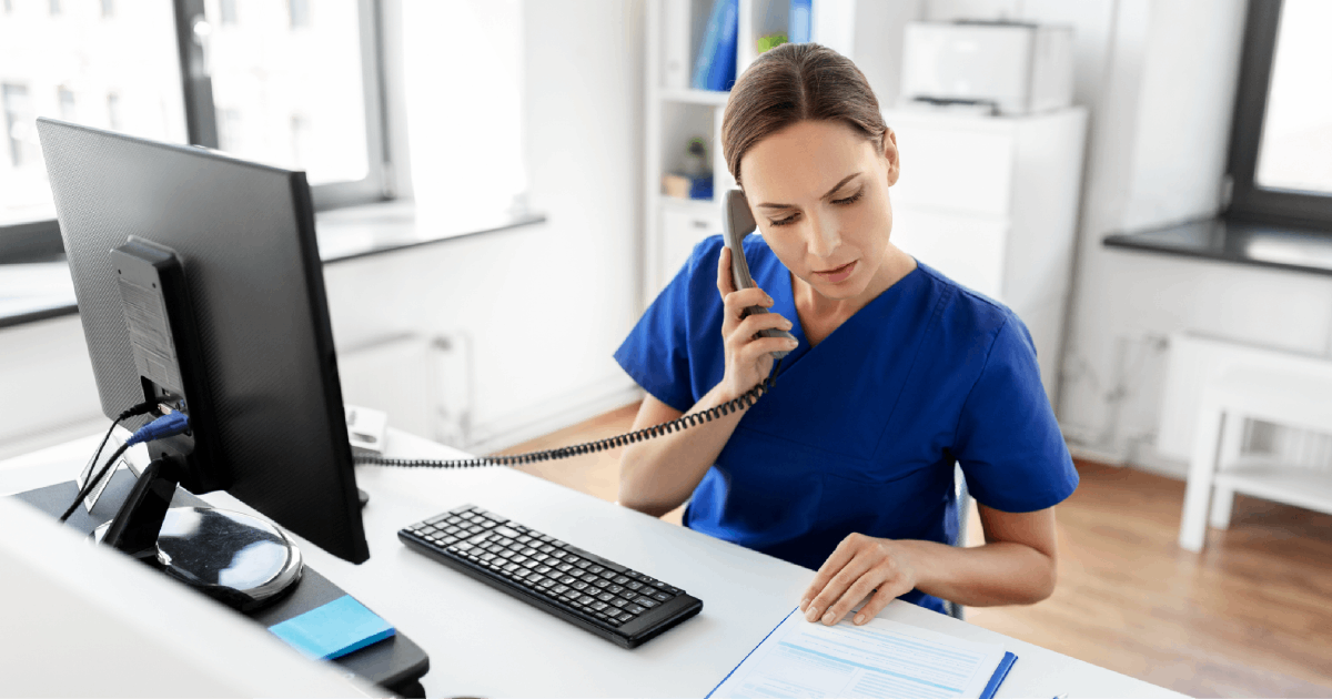 A female healthcare employee in scrubs answers the phone.
